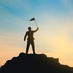 Silhouette of person standing on hilltop holding up a flag